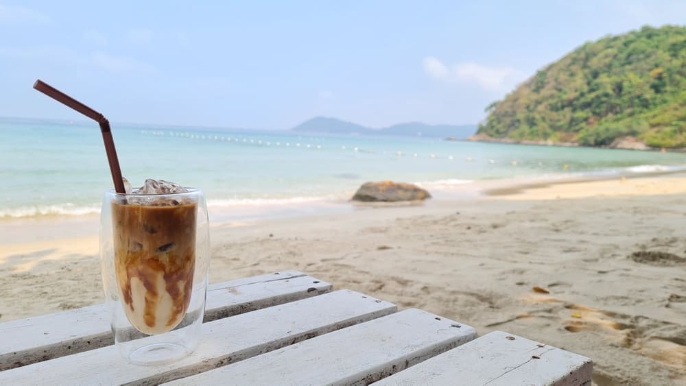 a refreshing ice coffee sitting atop a white table on a beach in Phuket, Thailand